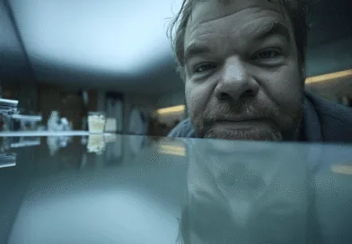 En medelålders man ses närbild vid ett spegelblankt bord. Miljön är en modern och stilren inomhusmiljö. Midcent. Teknik.