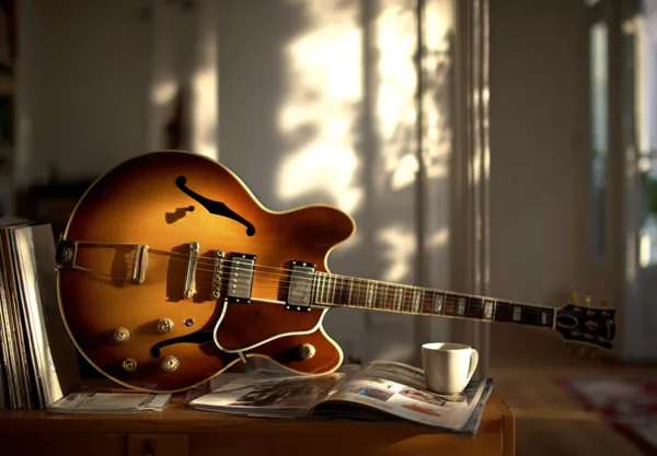 Midcent presenterar en stilren livsstilsmiljö med en vacker gitarr, vinylskivor och en kaffekopp. Denna bild fångar kreativitet och avslappning i hemmet. Kategori: Underhållning.
