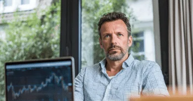 En medelålders man sitter vid ett skrivbord med fokus på en datorskärm som visar aktiemarknadsdata. Bilden illustrerar finansiell analys och investeringsplanering. Midcent. Kategori: Ekonomi.