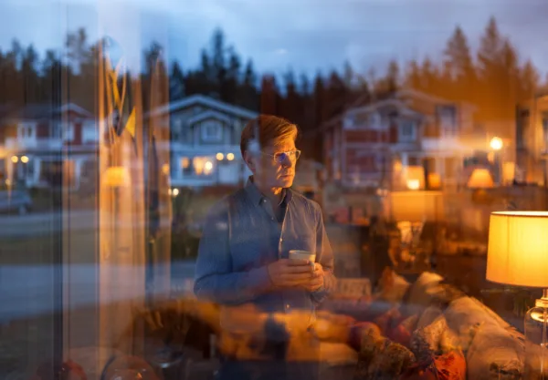 Midcent erbjuder en lugn och reflekterande atmosfär, perfekt för tankar och avkoppling. En medelålders man står vid fönstret med en kopp i handen, omgiven av varm belysning.Kategori: Samhälle.