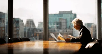 Midcent: En medelålders man läser dokument vid ett konferensbord i ett solbelyst kontor med stadsvy. Perfekt för att illustrera affärsstrategi och professionellt beslutsfattande. Ekonomi.