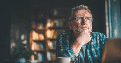 Midcent: En medelålders man sitter i ett bibliotek, djupt försjunken i tankar. Omgiven av böcker, med en kopp kaffe framför sig, ser han fundersam ut. Perfekt atmosfär för kreativt arbete och reflektion. Kategori: Samhälle.