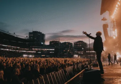 Midcent Underhållning. Bilden visar en medelålders man på en upplyst scen inför en stor folkmassa under en konsert. Stämningen är elektrisk med en vacker solnedgång i bakgrunden, vilket gör detta till en oförglömlig musikupplevelse.