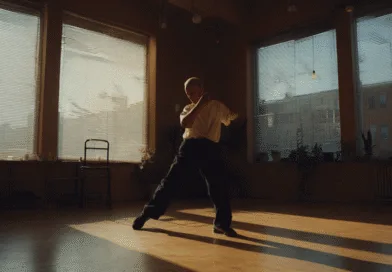 Midcent: En medelålders man utför Tai Chi i en ljus träningslokal med stora fönster. Harmonisk atmosfär och fokus på inre balans och välbefinnande. Kategori: Hälsa.