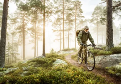Midcent: En medelålders man cyklar genom en dimmig skog, omgiven av höga träd och frodig grönska. Scenen utstrålar friluftsliv och äventyr. Perfekt bild för att inspirera till naturutflykter och aktivt liv. Kategori: Hä
