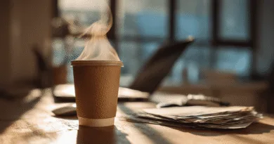 Midcent: En kaffekopp på ett solbelyst kontorsbord med ångande dryck, bredvid dokument och en laptop, vilket skapar en atmosfär av produktivitet och arbetsmiljö. Passar bra för beskrivning av modern arbetsplatskultur. Kategori: Arbetsliv.