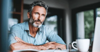 Midcent, en medelålders man, sitter vid ett bord med en kaffekopp, fundersam och reflekterande i en modern miljö. Bilden fångar en lugn och introspektiv stund. Kategori: Samhälle.