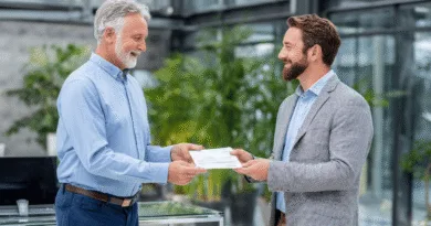 Midcent: En medelålders man och en bearded man i elegant kontorsmiljö utbyter dokument. Affärsklädda, de uttrycker professionell samarbete och förtroende. Ekonomi.