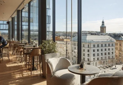 Midcent. Panoramautsikt över en stadsdel från ett elegant kafé med en medelålders man vid bardisken. Modernt interiördesign med stora fönster och träelement. Perfekt för avkoppling eller arbete.Kategori: Resa.