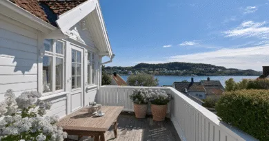 Midcent: En vacker terass med panoramautsikt över stilla vatten och blomsterprydd inredning. Stora trähus i bakgrunden. Perfekt för avkoppling och njutning av natursköna vyer. Kategori: Resa.