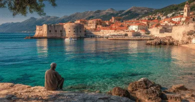 Midcent presenterar en medelålders man som blickar ut över det pittoreska landskapet vid kusten med turkost vatten och historiska byggnader i bakgrunden. En perfekt vy för dem som älskar att utforska vackra destinationer. Kategori: Resa.