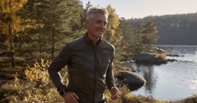 Midcent: En medelålders man joggar genom en höstfärgad skog vid en sjö, vilket skapar en känsla av frihet och hälsa. Solens strålar reflekteras i vattnet, vilket ger en inspirerande stämning. Kategori: Hälsa.