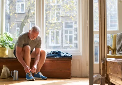 Midcent: En medelålders man knyter sina träningsskor i ett solbelyst rum. Växter och trädetaljer skapar en varm atmosfär. Aktiv livsstil och hälsa betonas. Kategori: Hälsa.