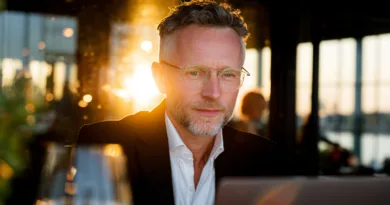 En medelålders man med glasögon arbetar fokuserat vid en laptop i solnedgången. Miljön är elegant och professionell, vilket understryker en känsla av framgång och beslutsamhet. Midcent – Ekonomi.