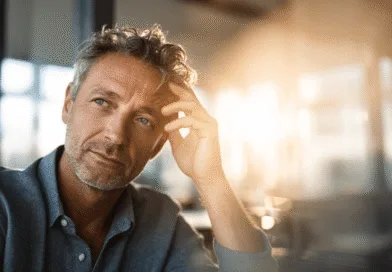 Midcent: En medelålders man sitter tankfullt med handen på huvudet i mjukt solljus. Bilden förmedlar eftertänksamhet och mognad, vilket kan inspirera till reflektion och introspektion. Idealisk för artiklar om personlig utveckling.Kategori: Samhälle.