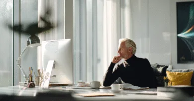 Midcent Ekonomi: En medelålders man sitter vid ett modernt kontorsbord, försjunken i tankar framför en dator. Det strömmar in naturligt ljus genom stora fönster, vilket skapar en inspirerande och produktiv arbetsmiljö.