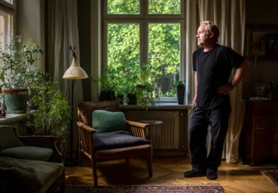 Midcent: En vuxen man står i ett ljust rum omgiven av växter, vilket skapar en lugn atmosfär. Kategorin är Samhälle.