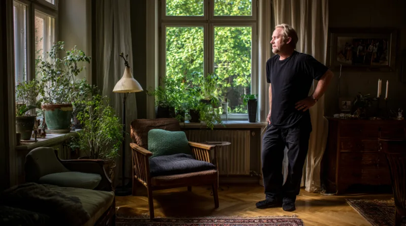 Midcent: En vuxen man står i ett ljust rum omgiven av växter, vilket skapar en lugn atmosfär. Kategorin är Samhälle.