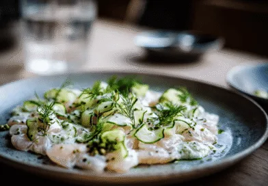 Midcent erbjuder en fräsch och läcker maträtt med skivad fisk, garnerad med krispig gurka och dill. Elegant uppläggning gör det till en visuell njutning, perfekt för finsmakare. Mat.