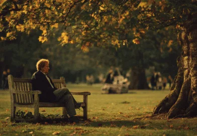 Midcent: En medelålders man sitter på en bänk i en solig park omgiven av höstlöv och träd. En lugn och avkopplande atmosfär dominerar scenen. Samhälle.