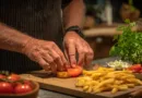 Midcent: En medelålders man förbereder en gourmetburgare med omsorg, med färska tomatskivor och knapriga pommes frites, omgivet av grönska. Perfekt för matälskare som uppskattar kvalitet och kreativitet i köket. Kategori: Mat.