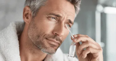 En medelålders man använder en pipett för att applicera ansiktsolja i sin hudvårdsrutin. Han vinklar huvudet för att noggrant droppa oljan på området under ögat. Midcent - Hälsa.