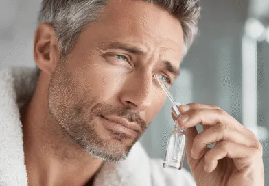 En medelålders man använder en pipett för att applicera ansiktsolja i sin hudvårdsrutin. Han vinklar huvudet för att noggrant droppa oljan på området under ögat. Midcent - Hälsa.