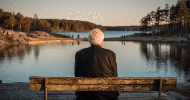 Midcent: En äldre man sitter på en parkbänk vid en stilla sjö, omgiven av natur och skog. Bilden fångar en känsla av lugn och reflektion i solnedgångens mjuka sken. Kategori: Samhälle.