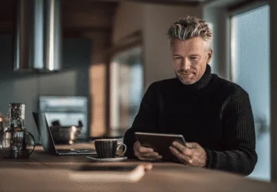 Midcent: En medelålders man i en modern miljö med laptop och surfplatta. Fokus på teknik och digital interaktion. Naturligt ljus från stora fönster ger en avslappnad atmosfär för arbetet. Kategori: Teknik.