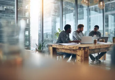 Midcent: En grupp vuxna män diskuterar projekt i ett modernt kontorsutrymme med stora fönster och växter, vilket skapar en inspirerande arbetsmiljö. Kategori: Teknik.