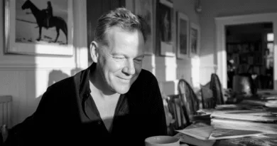 Midcent: En medelålders man sitter vid ett bord omgivet av böcker och tidningar. Solens sken skapar en avslappnad atmosfär i rummet. Han ser nöjd ut med en kopp kaffe. Kategori: Samhälle.