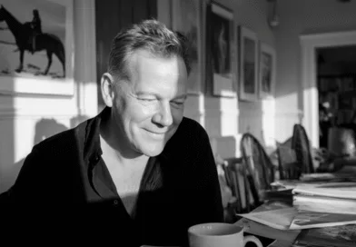 Midcent: En medelålders man sitter vid ett bord omgivet av böcker och tidningar. Solens sken skapar en avslappnad atmosfär i rummet. Han ser nöjd ut med en kopp kaffe. Kategori: Samhälle.