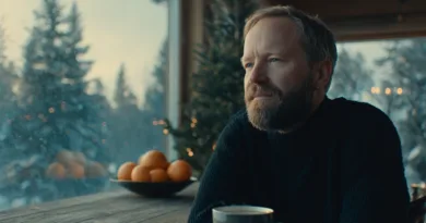 En medelålders man ser tankfullt ut genom ett fönster. Ute är det vintrigt med snöbeklädda träd. På bordet står en skål med