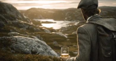 Midcent: En medelålders man klädd i vintage tweeddräkt beundrar ett storslaget landskap medan han håller ett whiskyglas. Bilden förmedlar äventyr och reflektion vid en skandinavisk utsikt.Kategori: Resa.