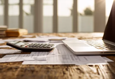Midcent Ekonomi: Ett kontorsbord med bärbar dator och miniräknare bland papper och dokument, perfekt för ekonomiska