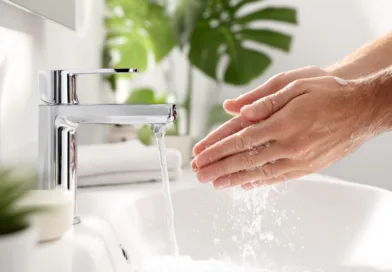 Midcent: En medelålders man tvättar händerna under rinnande vatten i ett modernt badrum. Handhygien och renlighet prioriteras mot en bakgrund av fräscha, gröna växter. Kategori: Hälsa.