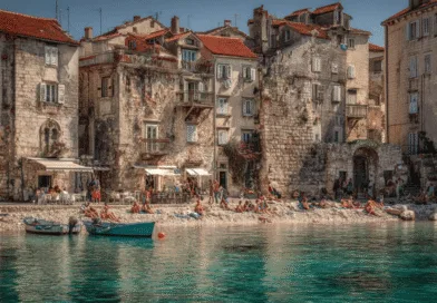 Midcent: Vackra stenbyggnader pryder stranden där människor njuter av solbad vid det kristallklara vattnet. Charmig kustatmosfär i historisk stadsmiljö inbjuder till avkoppling och utforskning. Perfekt resmål för kultur- och naturskönhetsäl