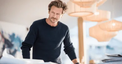 En medelålders man med fokusblick står i ett ljust kontorsutrymme, omgiven av papper. Midcent. Kategori: Samhälle.