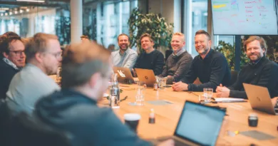 Midcent samlar en grupp medelålders män i ett modernt konferensrum. De diskuterar och samarbetar energiskt, omgivna av teknologi och en produktiv atmosfär. Kategorin för denna bild är Samhälle.