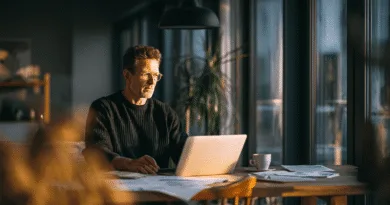 En medelålders man sitter fokuserat vid ett laptopbord i varma ljusförhållanden. Omringad av papper och en kaffekopp, skapar han en produktiv atmosfär. Bilden utstrålar professionalism och reflektion.Midcent, Ekonomi.