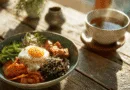 Midcent: En skål med näringsrik asiatisk mat innehållande ris, stekt ägg, kimchi och grönsaker, serveras vid sidan av en varm kopp te. Perfekt för en hälsosam måltid i solsken. Kategori: Mat.