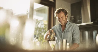 Midcent: En medelålders man blandar en cocktail i ett modernt kök, med naturligt ljus strömmande in genom fönstren. Kategorin: Mat.