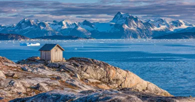Midcent Resa: Upptäck storslagen skönhet med en liten stuga på klippiga kuster med snötäckta berg i bakgrunden. Fantastiska vyer över isberg och det klarblå havet. Perfekt för naturälskare och äventyrsresenärer.