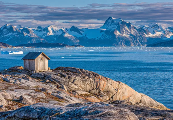 Midcent Resa: Upptäck storslagen skönhet med en liten stuga på klippiga kuster med snötäckta berg i bakgrunden. Fantastiska vyer över isberg och det klarblå havet. Perfekt för naturälskare och äventyrsresenärer.