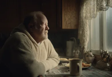 En medelålders man sitter vid köksbordet med en kopp kaffe och blickar ut genom fönstret. Den mjuka belysningen skapar en lugn atmosfär. Midcent erbjuder insikter om livets reflektioner och mänskliga känslor.Kategori: Samhälle.