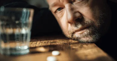 En medelålders man ser tankfull ut vid ett bord med ett glas vatten och två tabletter. Bilden fångar en känsla av reflektion och eftertanke. Midcent. Hälsa.