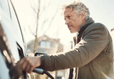 Midcent: En medelålders man laddar en elbil med soligt väder i bakgrunden, vilket framhäver grön teknik och hållbarhet. Bilden symboliserar framtidens transporter med fokus på miljövänliga alternativ. Kategori: Teknik.