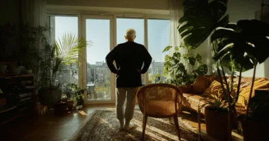 En medelålders man står i ett soligt rum med rika gröna växter och en modern inredning, vilket skapar en harmonisk atmosfär av välbefinnande och avkoppling. Midcent - Hem & Inredning.